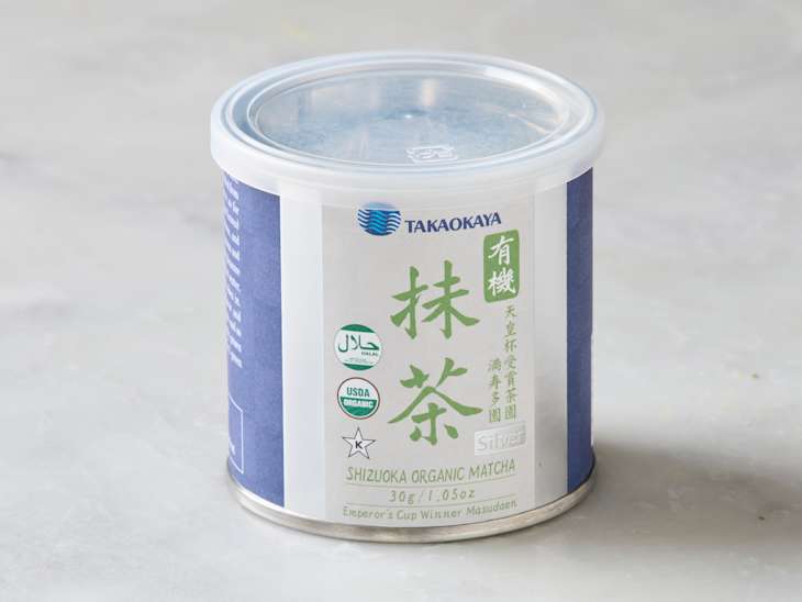 Container of Shizuoka organic matcha powder with a clear lid, featuring green and blue labeling and certification symbols.