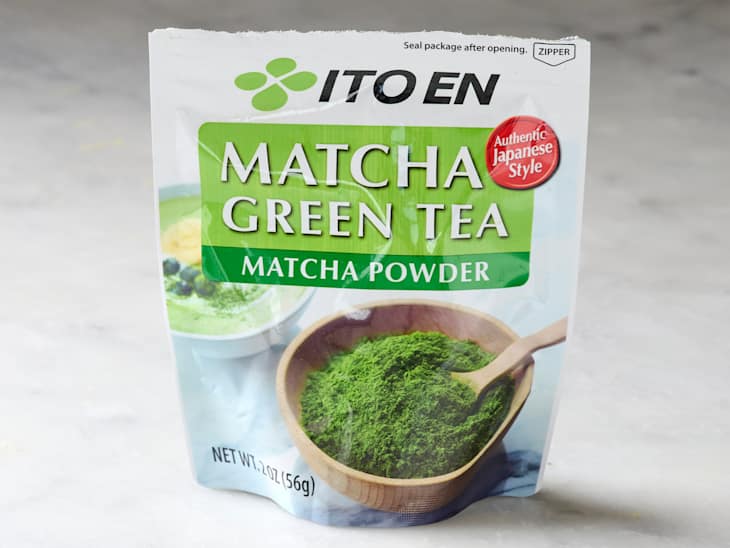 Matcha green tea powder package with a wooden bowl of matcha and a spoon, featuring a green and white design.