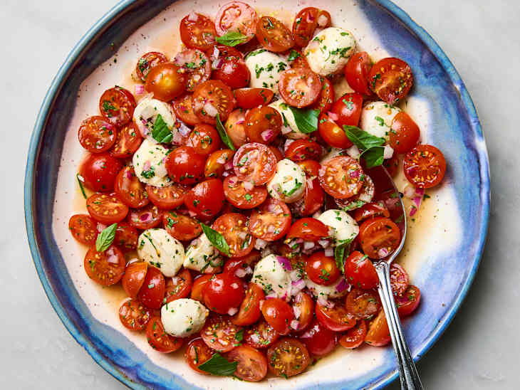 Fresh cherry tomatoes and mozzarella balls mixed with herbs and red onion in a blue-rimmed bowl.