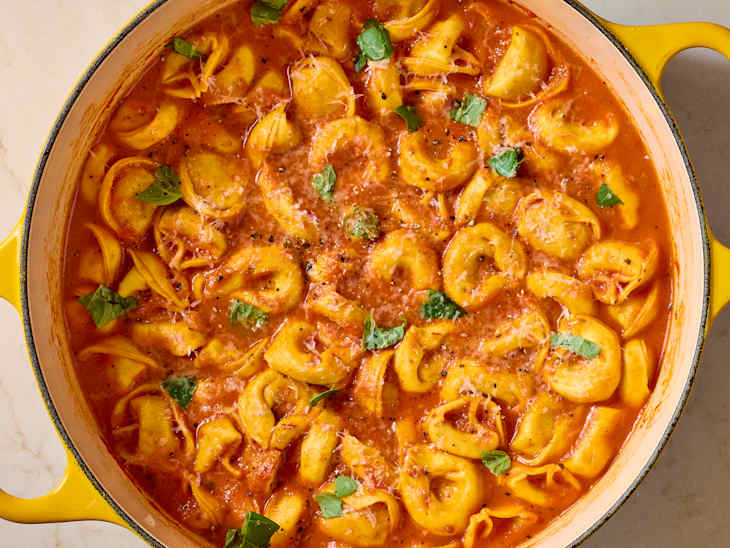 Creamy tortellini in a rich tomato sauce, garnished with fresh basil and black pepper in a yellow pot.