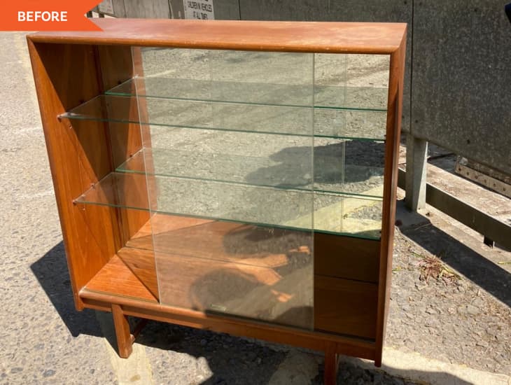 Wooden display cabinet with glass shelves and sliding doors, placed outdoors on a concrete surface.