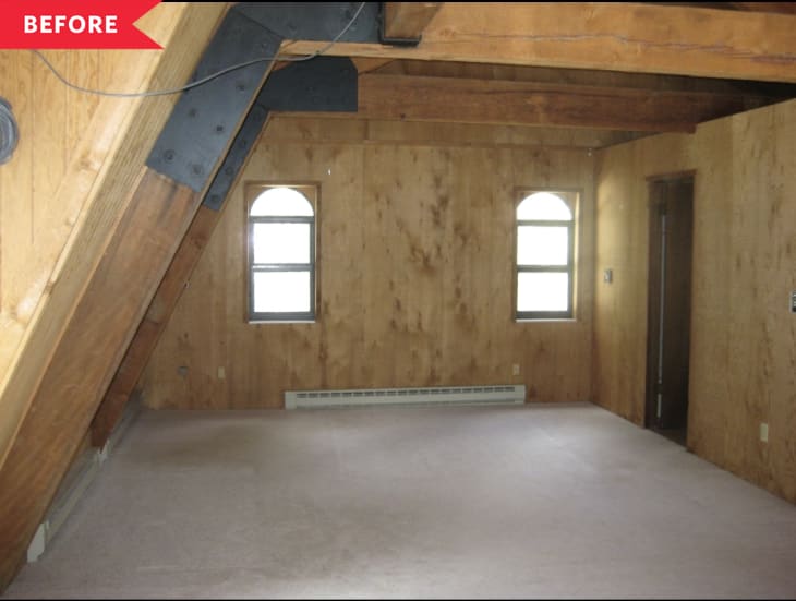 Empty attic room with wood-paneled walls, exposed beams, and two arched windows.