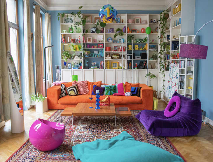 colorful blue and white living room with bright orange sofa and lots of tall built in bookshelves