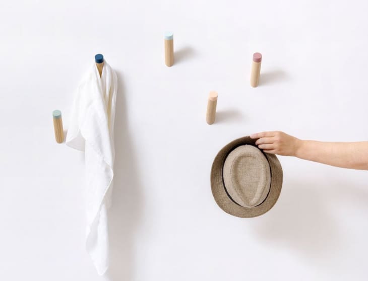 Hand placing a straw hat on a wall with colorful wooden pegs, one holding a white cloth.