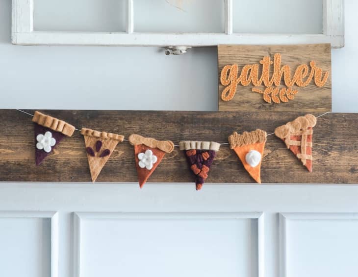 Felt pie slice garland with various toppings hanging on a wooden board, next to a "gather" sign.