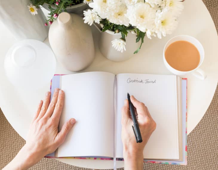 Hands writing in gratitude journal with cup of coffee on table