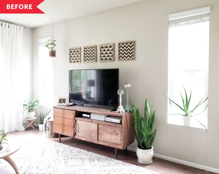 Living room with a wooden TV stand, potted plants, and geometric wall art above the television.