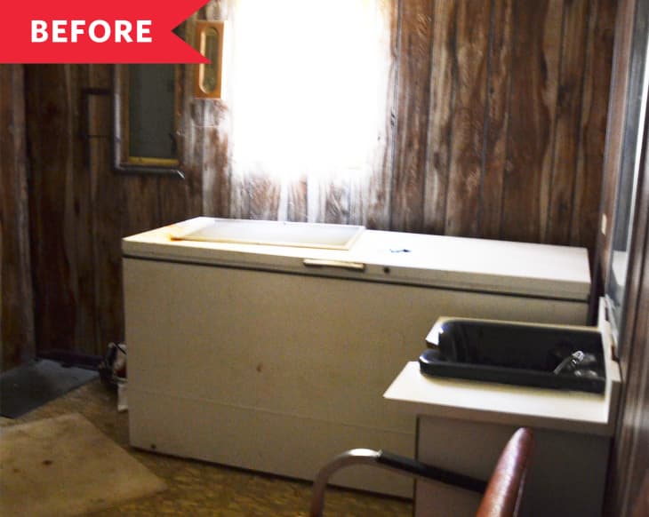 Wood-paneled room with a large white freezer, black sink, and red chair.