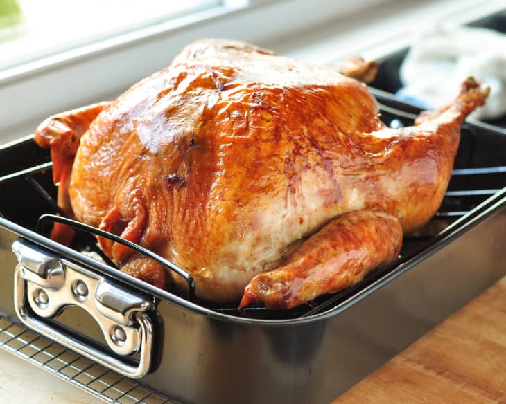 Golden roasted turkey in a black roasting pan on a wooden surface.