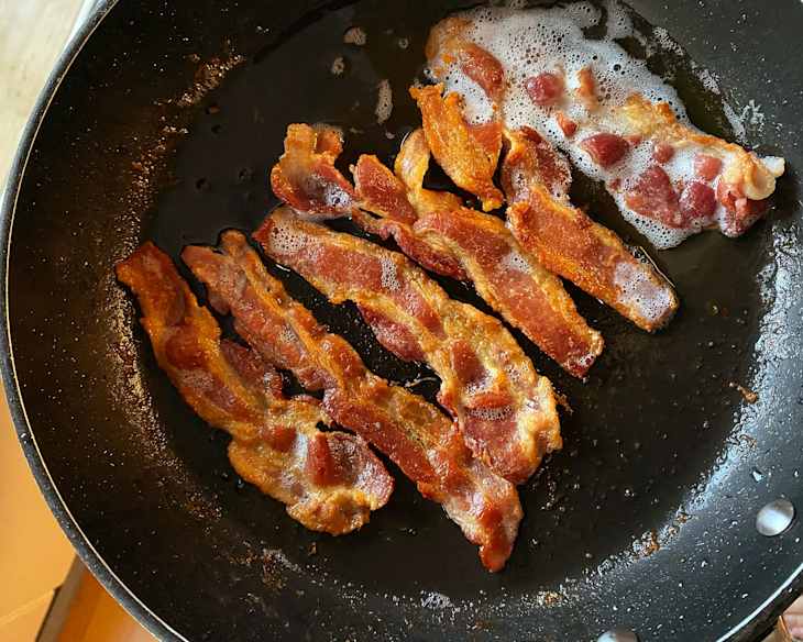 Bacon frying in skillet.