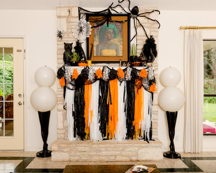 Halloween-themed fireplace with black, orange, and white garlands, large spider decor, and a framed portrait.