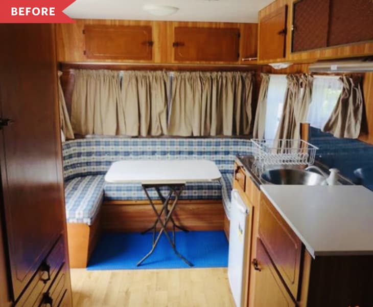 Camper interior with wood cabinets, blue checkered bench, white table, and small kitchen area.