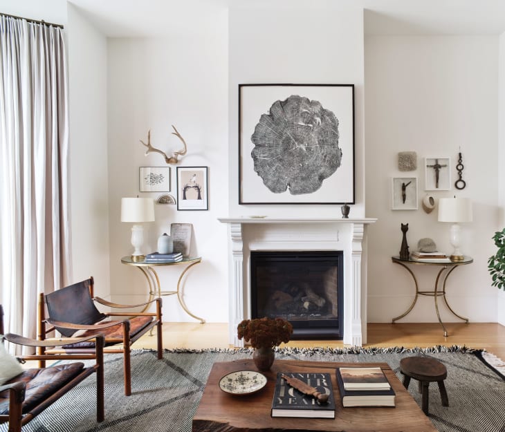 Living room with a white fireplace, abstract art, leather chairs, and a wooden coffee table with books and decor.