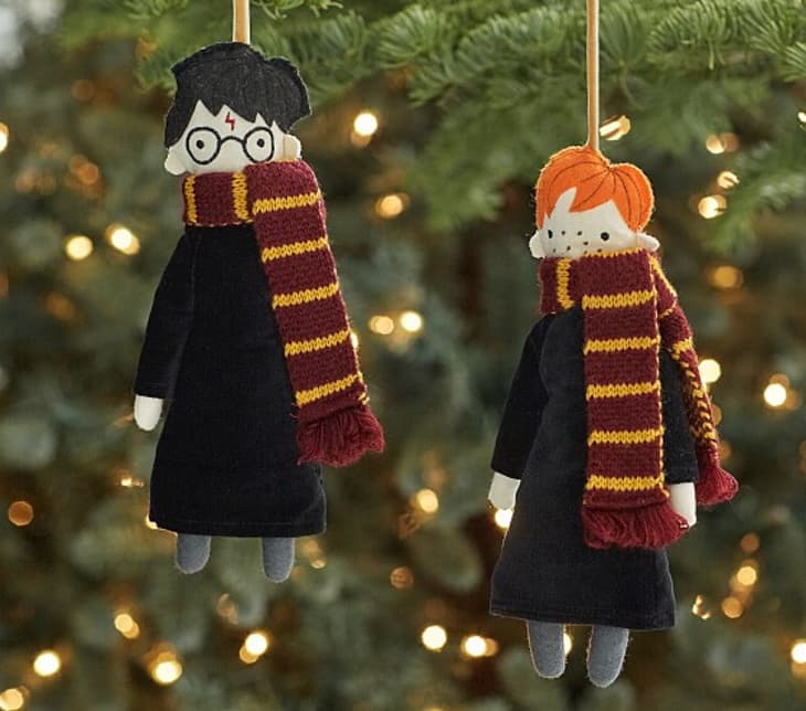 Two felt ornaments of characters with glasses and red hair, wearing striped scarves, hanging on a Christmas tree.