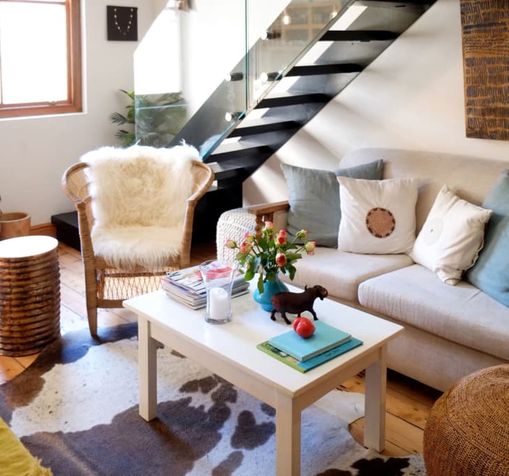 Cozy living room with a beige sofa, fluffy chair, cowhide rug, and a coffee table with flowers and books.