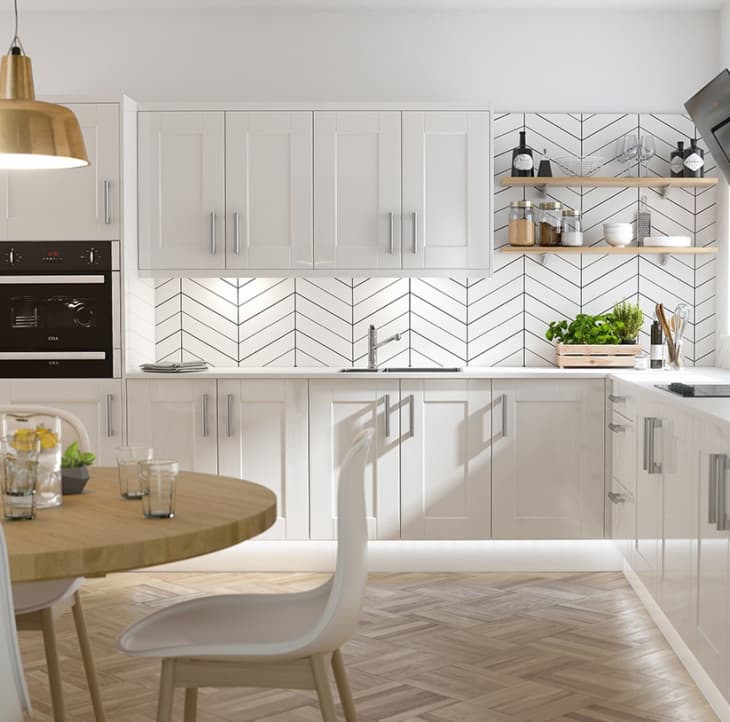 Modern kitchen with white cabinets, chevron backsplash, wooden shelves, and a round dining table with white chairs.