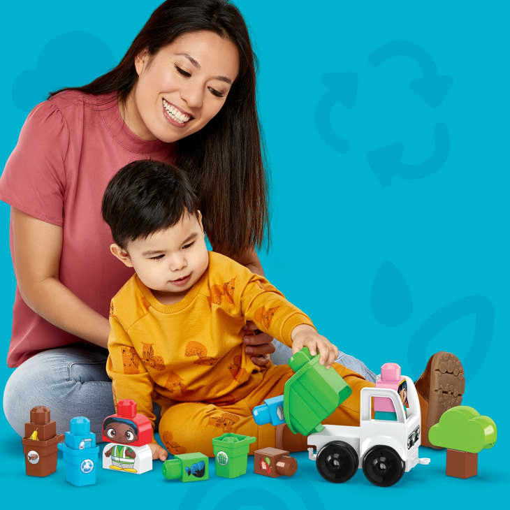 Woman and child playing with colorful recycling-themed toy blocks and truck.