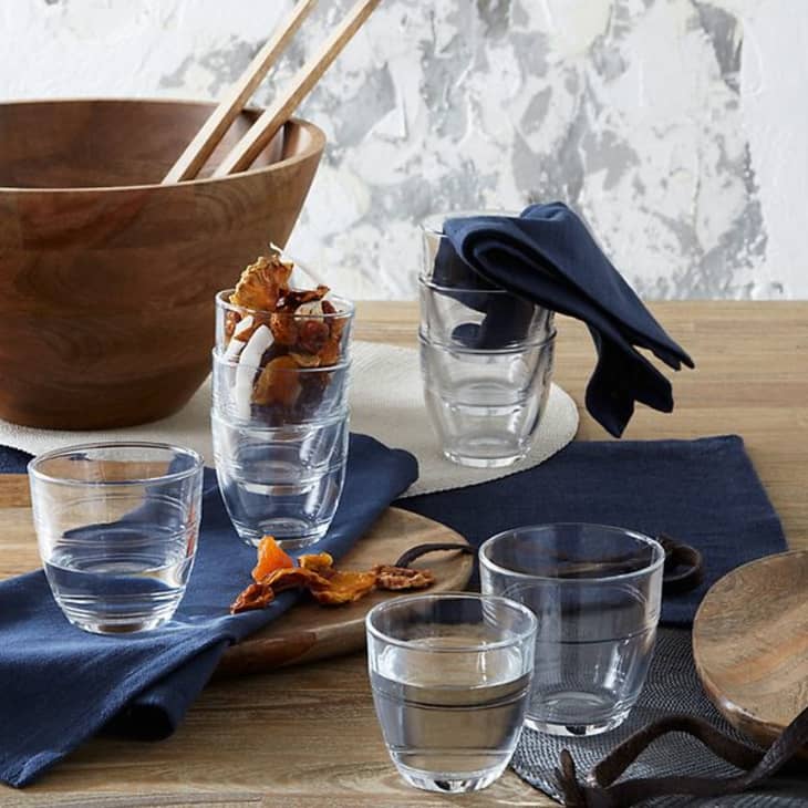 Simple, everyday drinking glasses by Duralex arranged on a table with a large salad bowl and cloth napkins