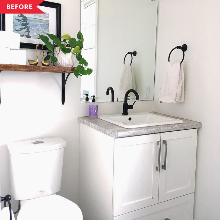 Small bathroom with white vanity, black faucet, large mirror, and wooden shelf with plants and decor.