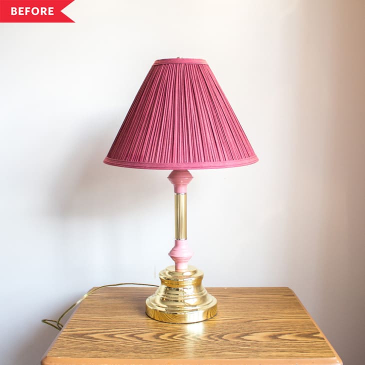 Brass table lamp with a pink pleated shade on a wooden surface.