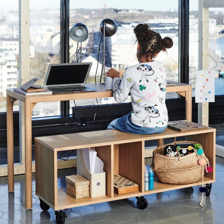 Girl sitting on oak veneer bench on casters, working at desk with laptop