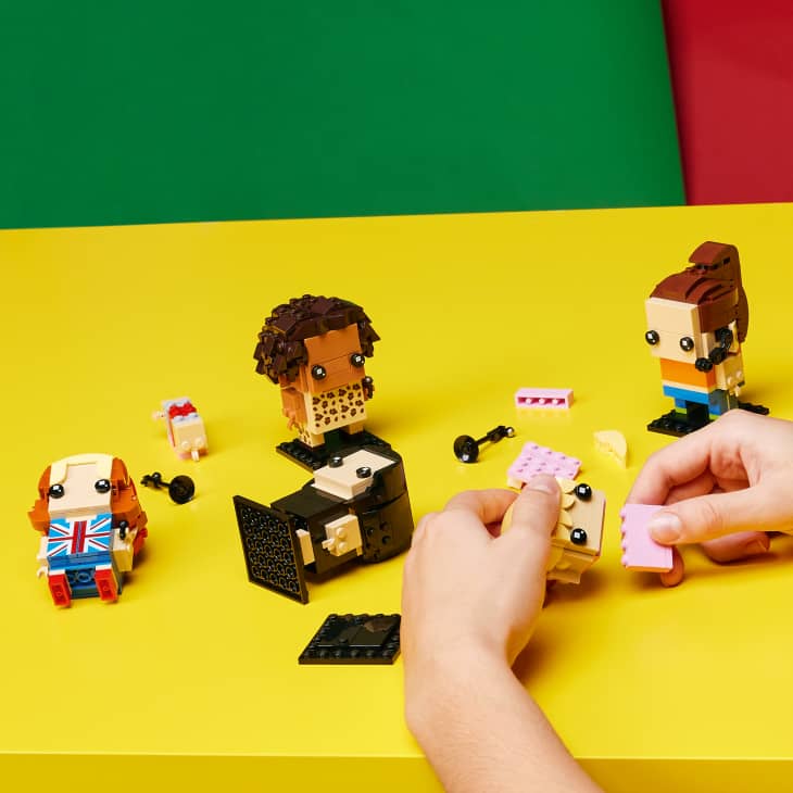 Hands assembling block figures on a yellow table with colorful background.