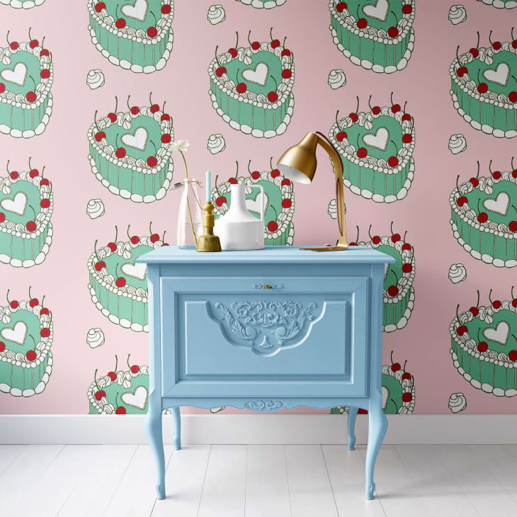 Blue vintage dresser with gold lamp and vases against pink cake-patterned wallpaper.