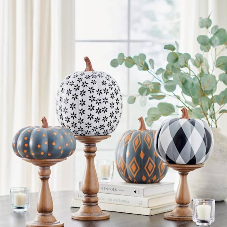 Decorative pumpkins with geometric patterns on wooden stands, surrounded by candles and books.