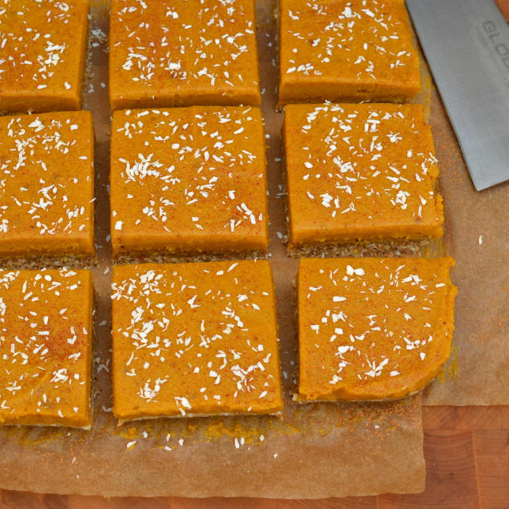 Image 3: Pumpkin bars topped with shredded coconut, cut into squares on parchment paper.