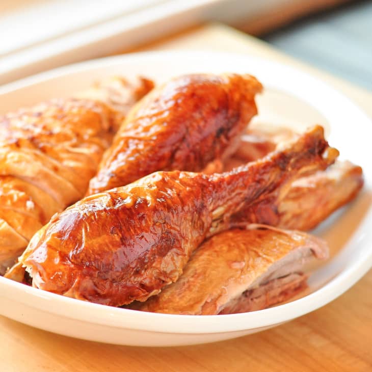 Roasted turkey drumsticks and breast slices on a white plate.