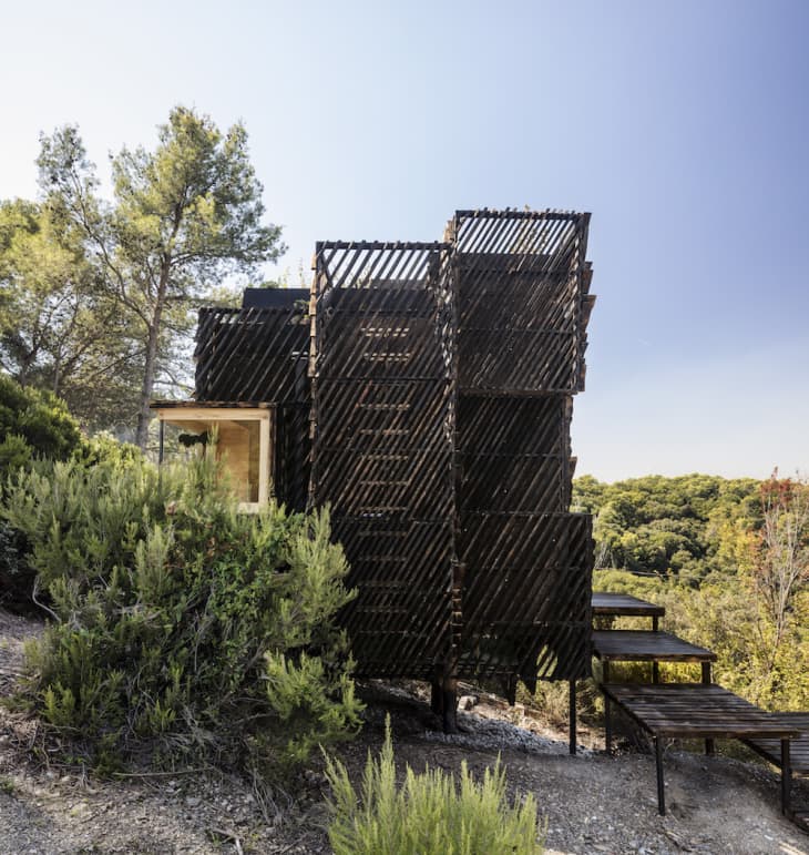 Modern wooden cabin with slatted exterior nestled in a forested hillside.