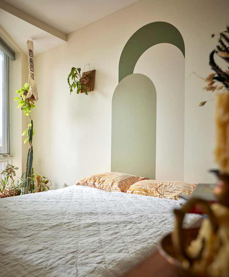 Bed against decoratively painted wall in sleeping area of studio apartment.