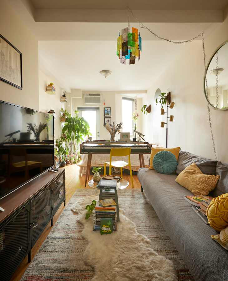 Main living area of studio apartment with colorful lamp and round mirror above couch.