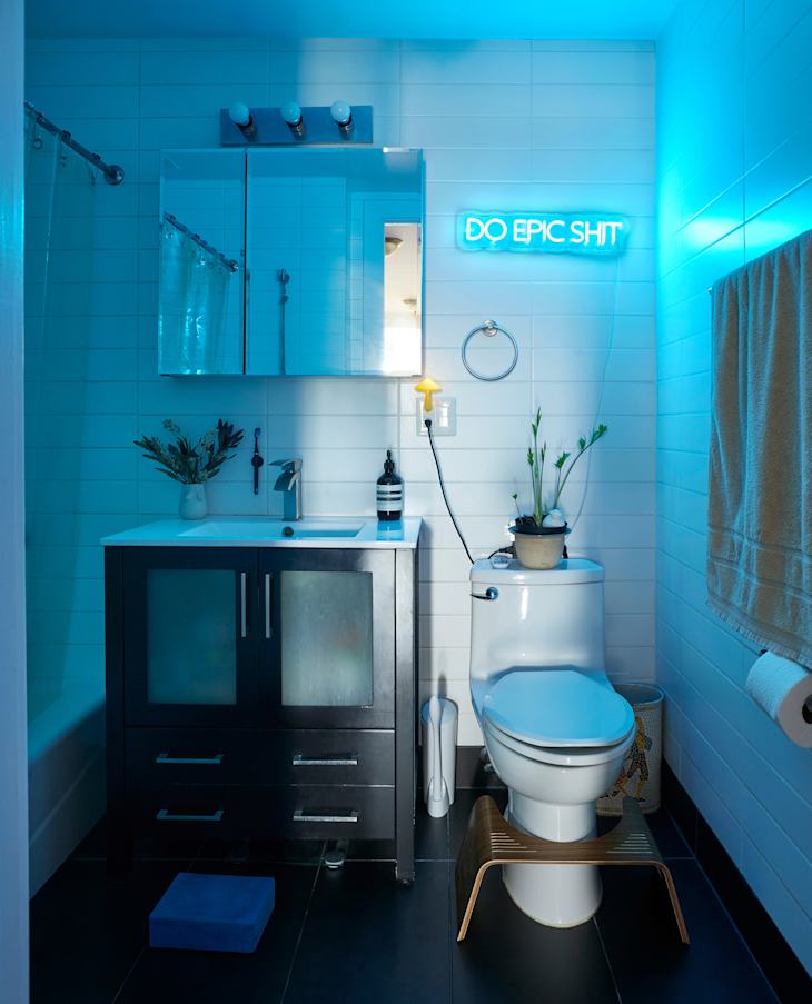 Neon light above toilet in white bathroom.