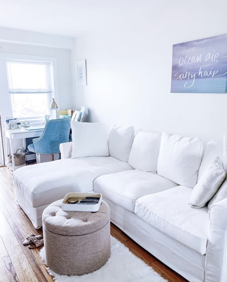 White sectional sofa in a bright room with a blue chair, desk, and wall art saying "Ocean air, salty hair."