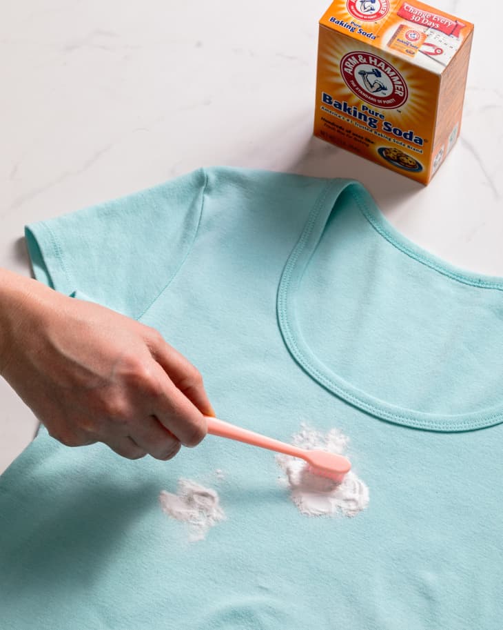 Using baking soda and a brush to scrub a grease stain on a blue t-shirt