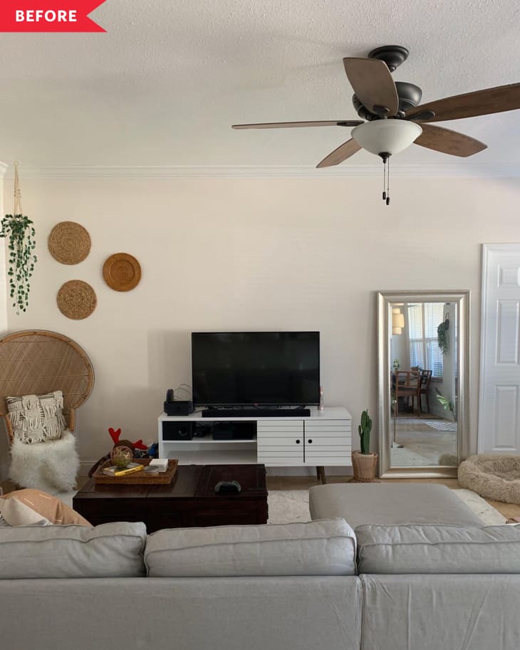 Living room with gray sofa, TV on white stand, wicker chair, wall baskets, ceiling fan, and large mirror.
