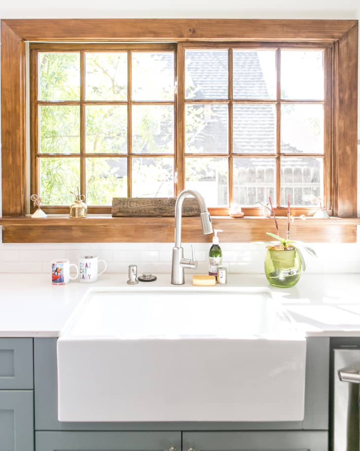 White kitchen sink with gray cabinets, white countertops, rustic wood-framed window