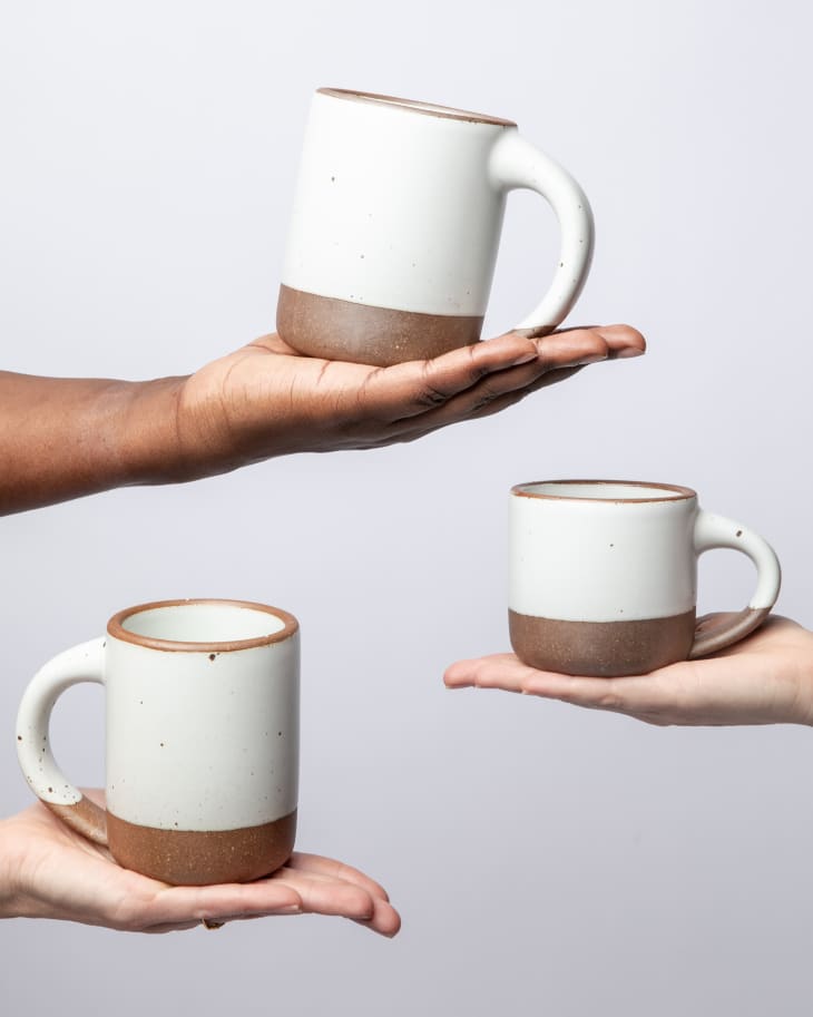 Three hands holding ceramic mugs with white tops and brown bases.