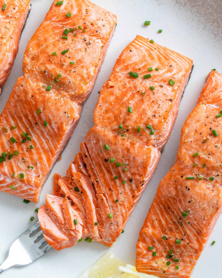 baked salmon garnished and a fork lays with piece of salmon