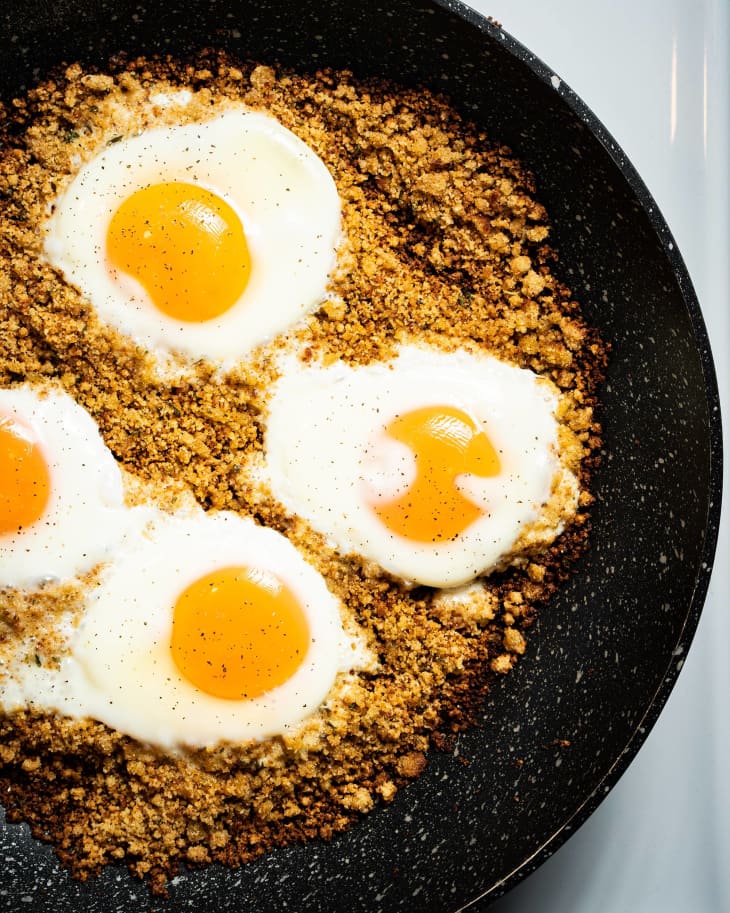 Fried eggs on bed of breadcrumbs in skillet.