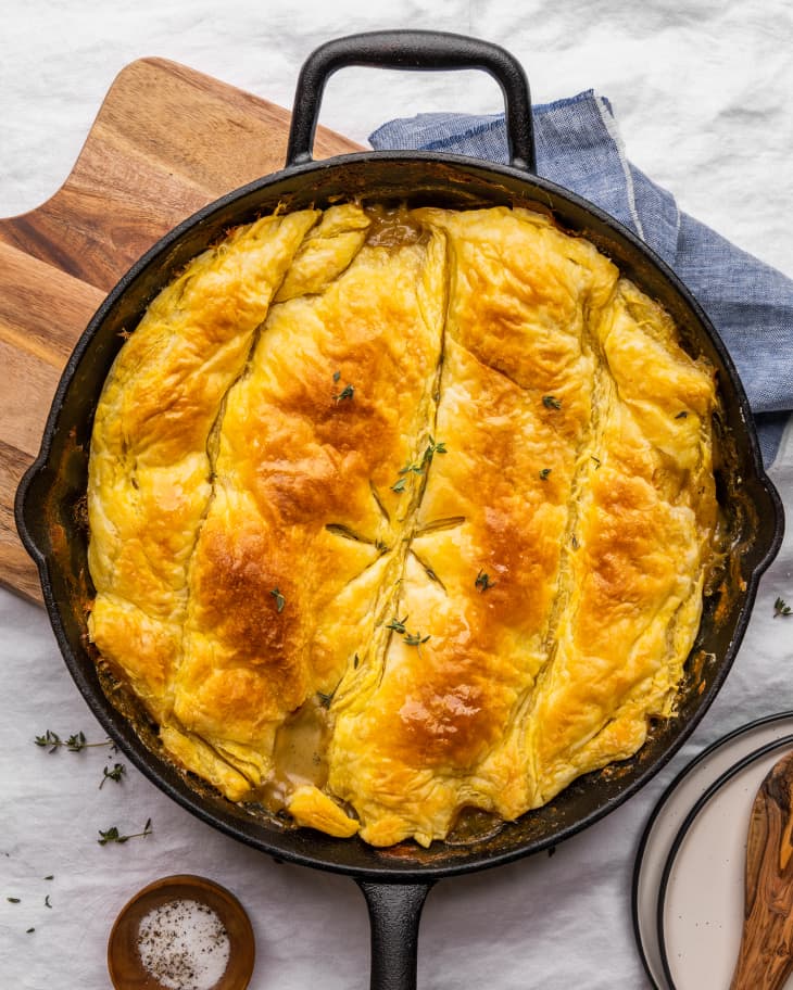 Golden puff pastry-topped vegetarian skillet pot pie with fresh thyme on a wooden board.