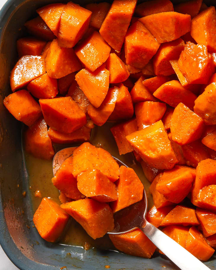 Close up view of a dark grey pan of candied yams with a spoon in the bottom left corner.