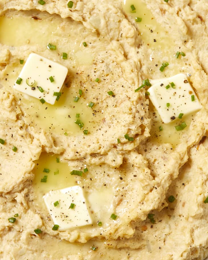 Close view of mashed potatoes topped with herbs and 3 pats of butter.