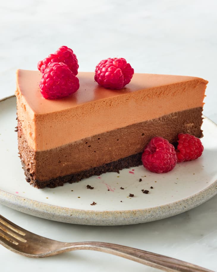 angled shot of a piece of triple chocolate mousse cake topped with raspberries.