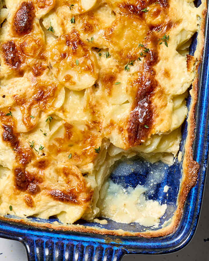 overhead shot of scalloped potatoes in a dark blue baking dish, with a large scoop taken from the bottom right corner.
