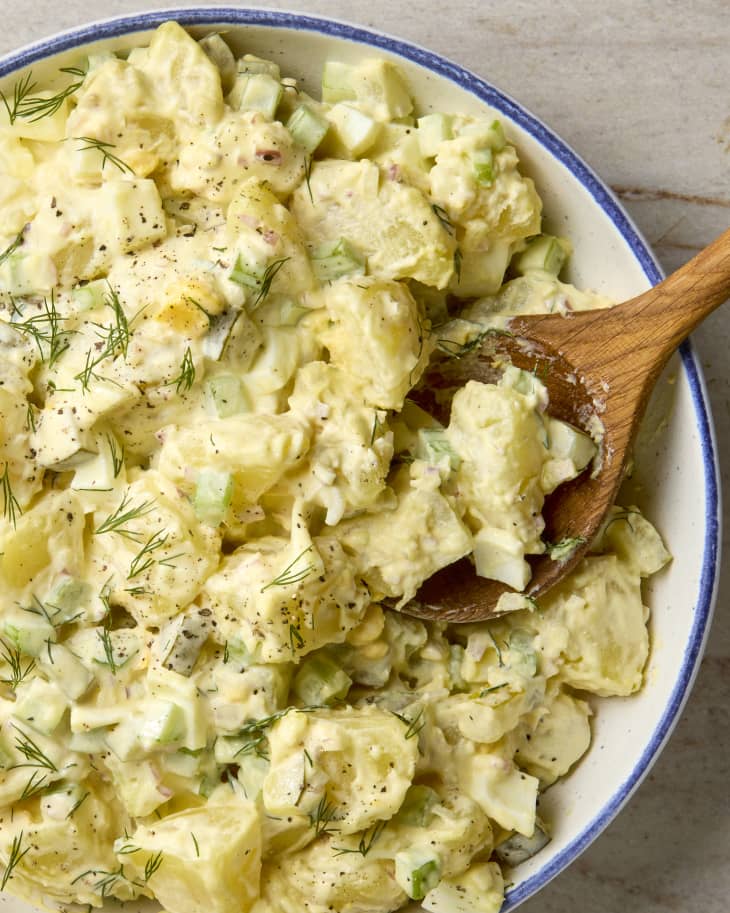 overhead shot of potato salad in a white bowl with a blue rim, topped with dill