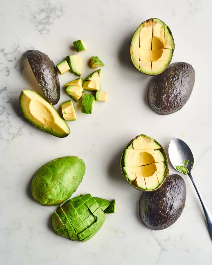 four avocados sit on a marble table peeled, diced, and laid out in different ways