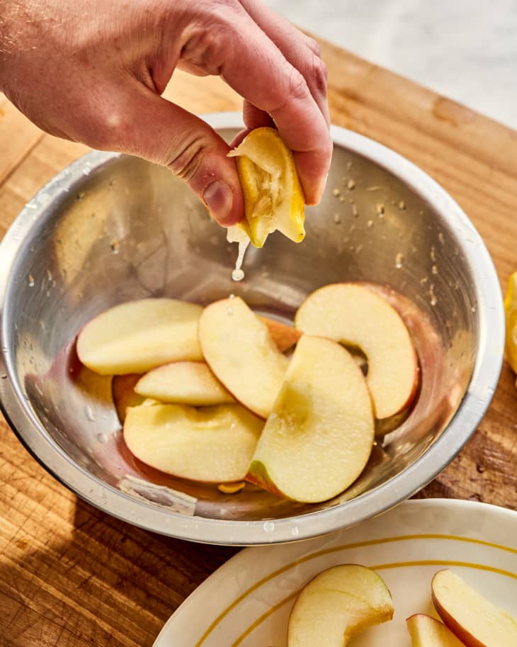 someone squeezing lemons into a bowl of apples