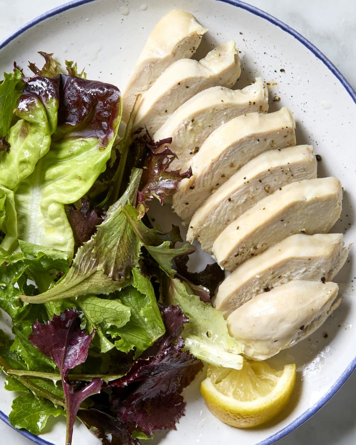 overhead shot of poached chicken on a plate with a side salad and lemon wedge.